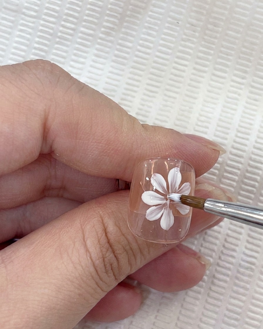 Three white petals painted on the nail, forming three quarters of a cross shape.