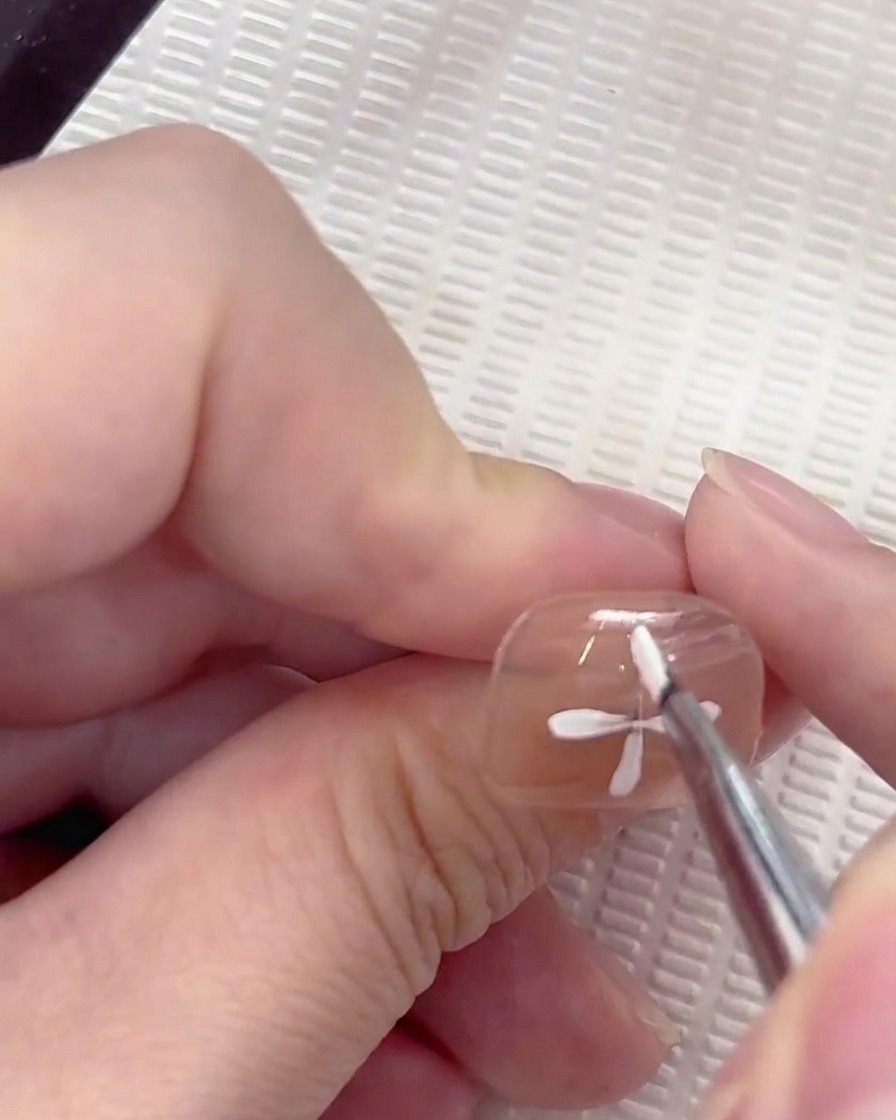 A fifth white petal being added into the gap between the established petals on the nail.