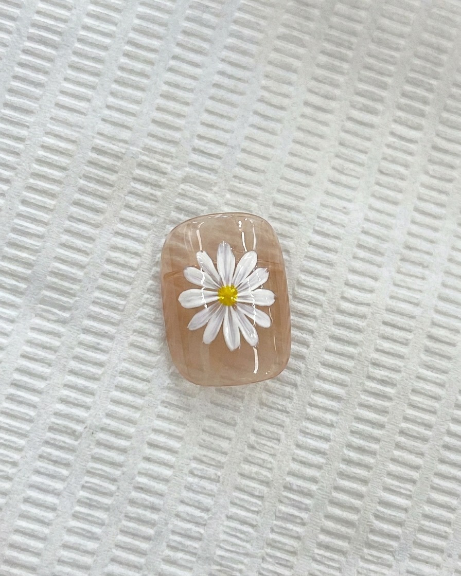 A close-up of a white daisy on a nail, with a fine detail brush applying a yellow center.