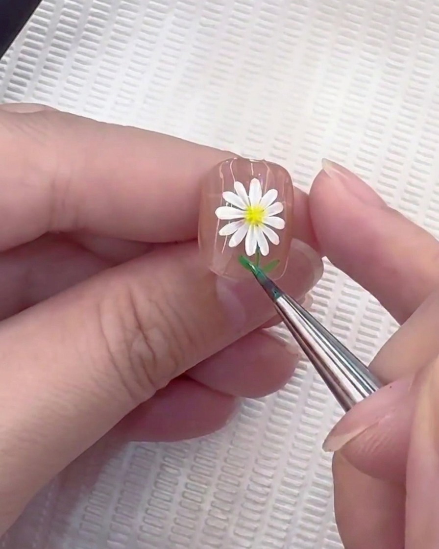A liner brush adding small green leaves to the base of a stem painted on a nail.