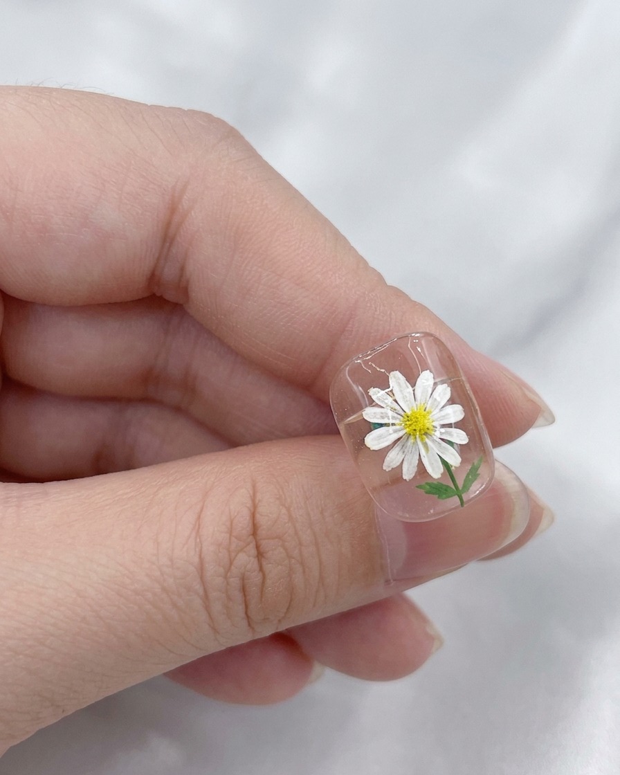 A brush applying a clear, glossy top coat over a finished daisy nail art design.