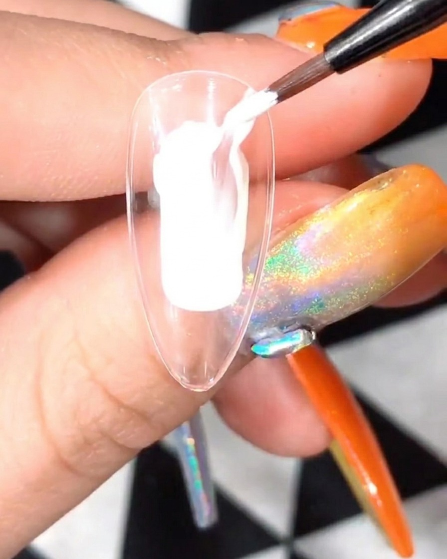 A clear nail tip with white petal art being cured inside a UV/LED nail lamp.