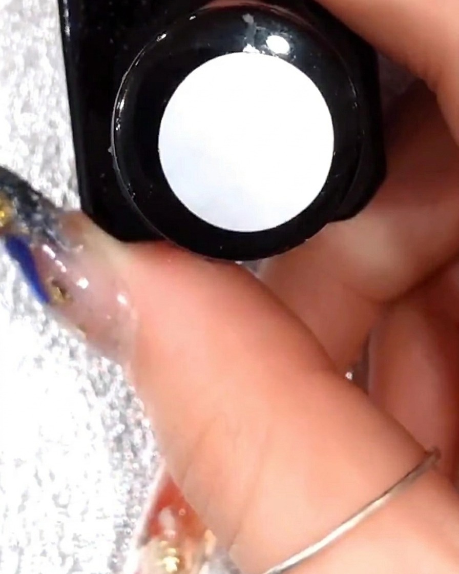 A close-up view of a brush applying a thin layer of clear gel over the existing white petal art.