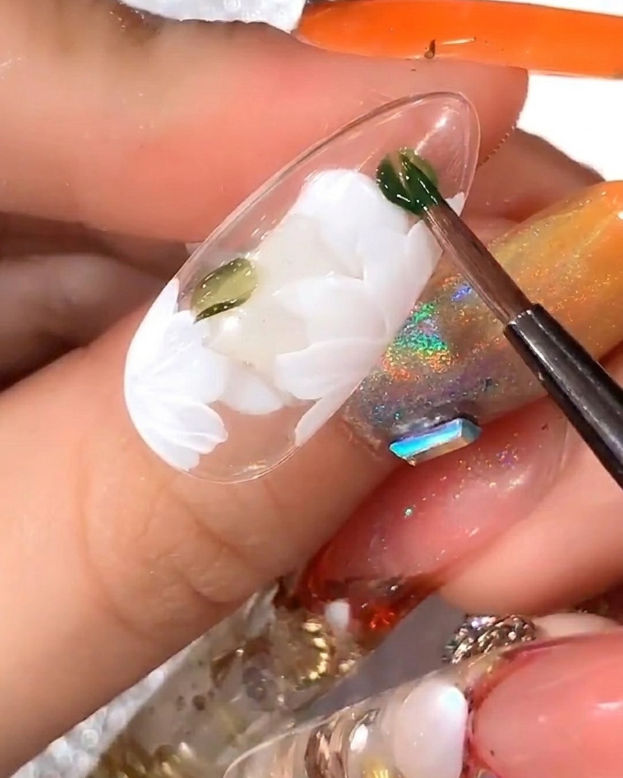 The tip of a brush placing a bright yellow dot in the center of the completed white daisy flower.
