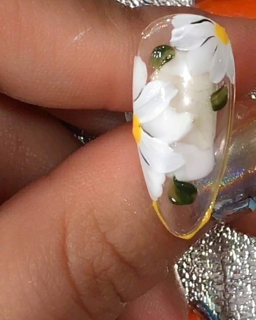 A brush applying a final coat of matte top gel over a nail featuring white daisy art and green leaves.