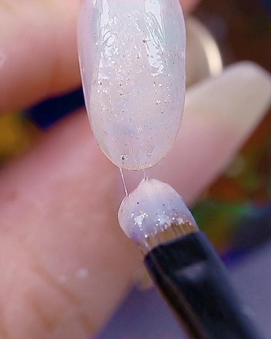 A nail brush applying a second layer of sugar-textured gel, with the nail surface appearing textured and ready for curing.