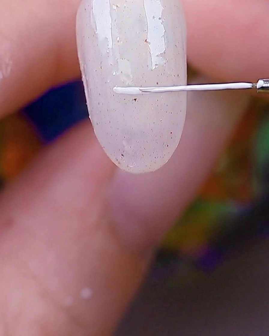 A detail shot of a thin liner brush tracing a white rectangular border on the corner of a textured nail.