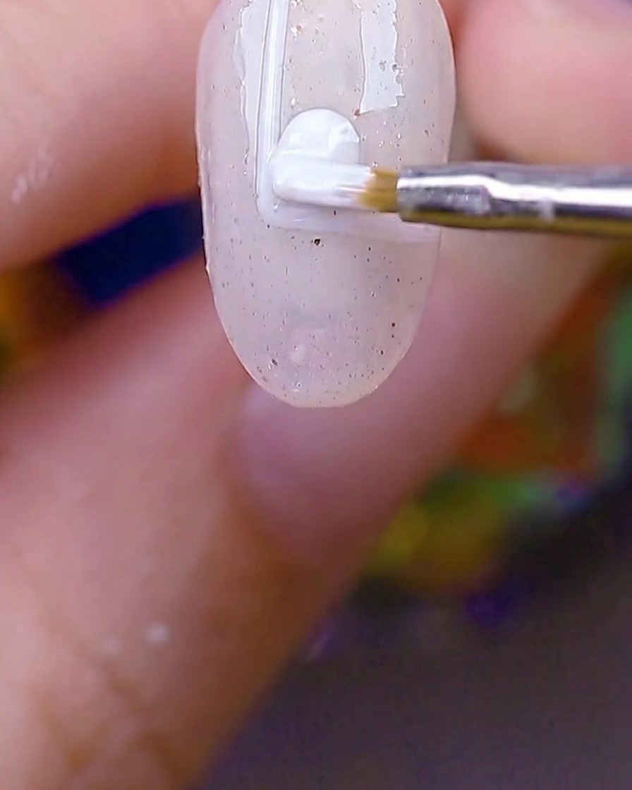 A small round brush filling in the white-bordered rectangle on the nail with opaque white gel.