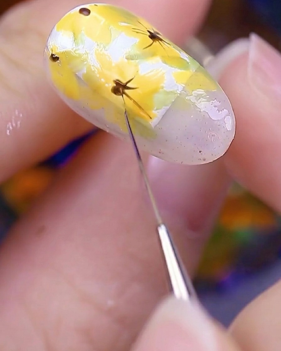 A close-up of the painted nail being held under a UV nail lamp to cure the freshly applied floral details.