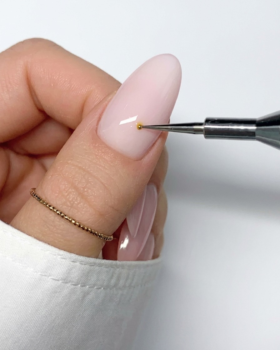 A thin nail art brush pulling a line of white gel polish outward from the yellow center dot.