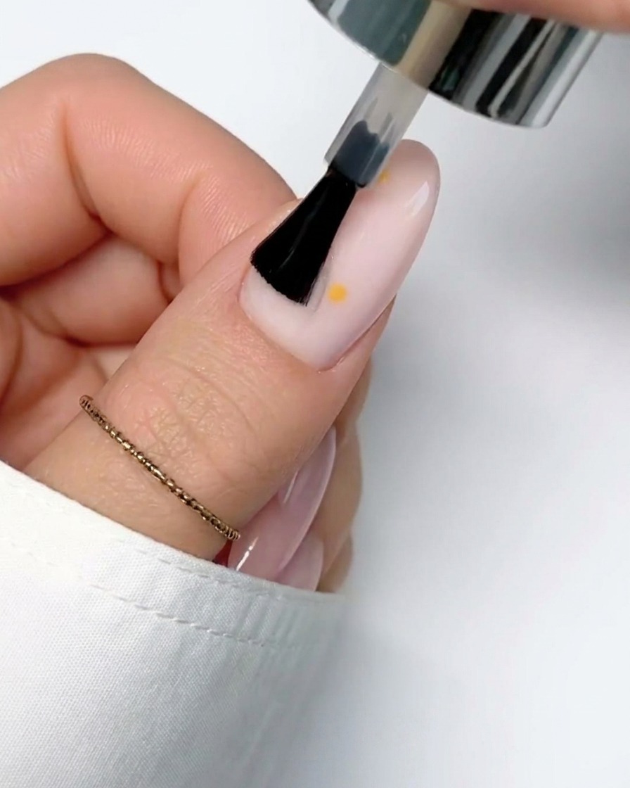 A thin brush adding a second white petal to the daisy design on the nail.