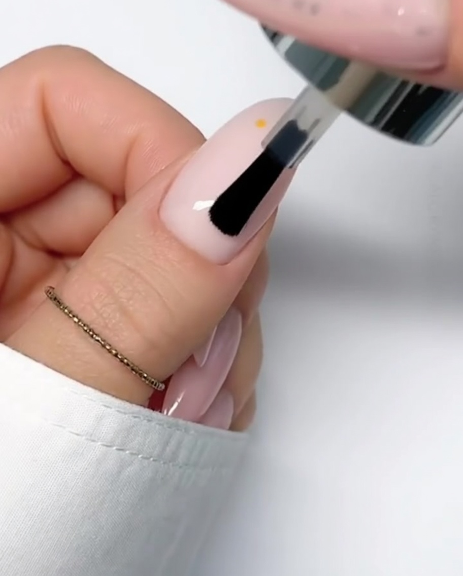 A thin brush applying the fourth white petal to the daisy flower design.