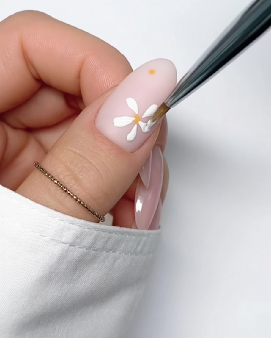 A close-up of a nude-colored nail with a small, perfectly round yellow gel dot applied to the surface, ready for petal painting.