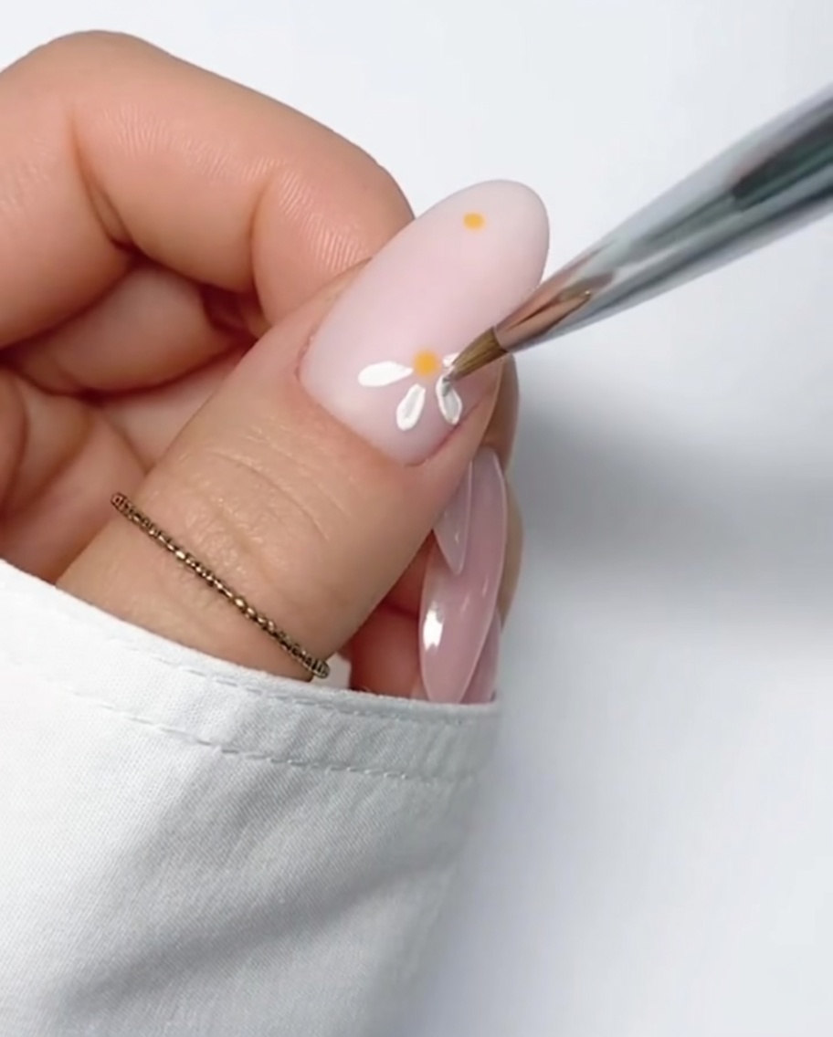 A fully formed white daisy with a yellow center painted on a nude nail background.