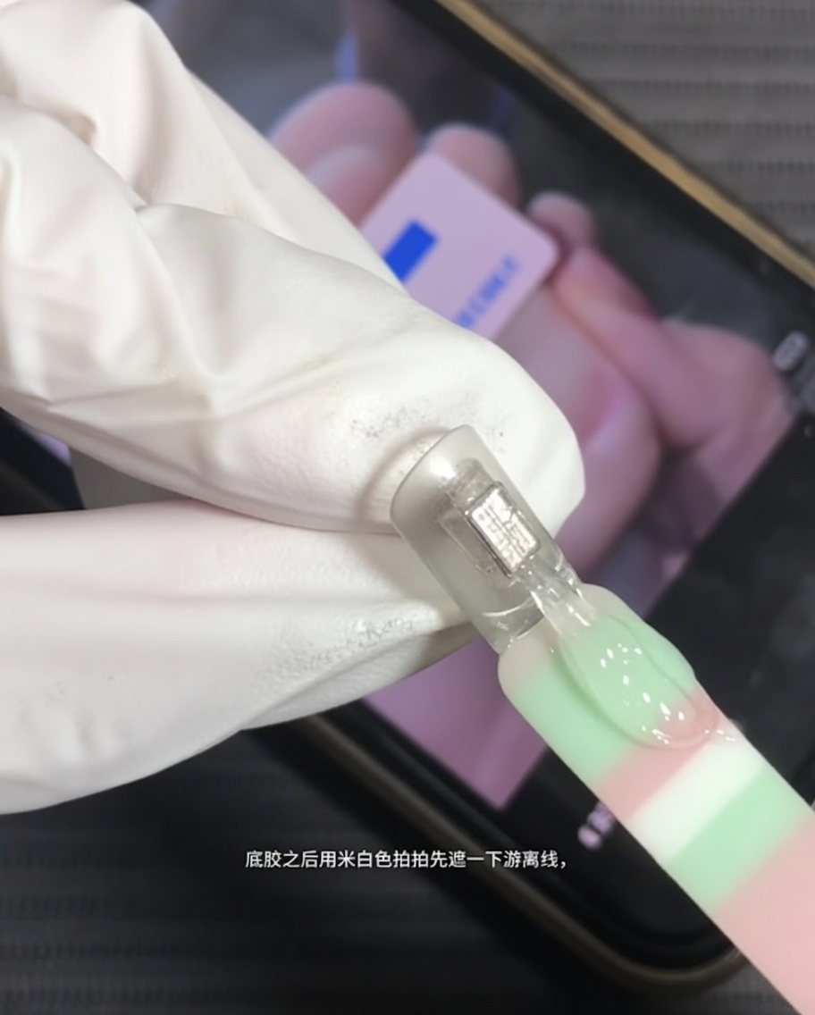 A brush applying milky white gel to the tip of a natural nail.