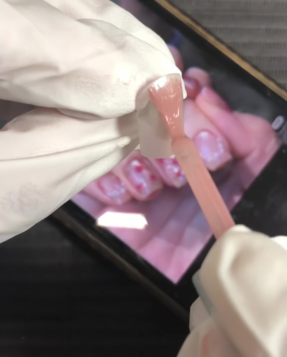 A brush applying nude pink gel polish to the entire surface of the nail.