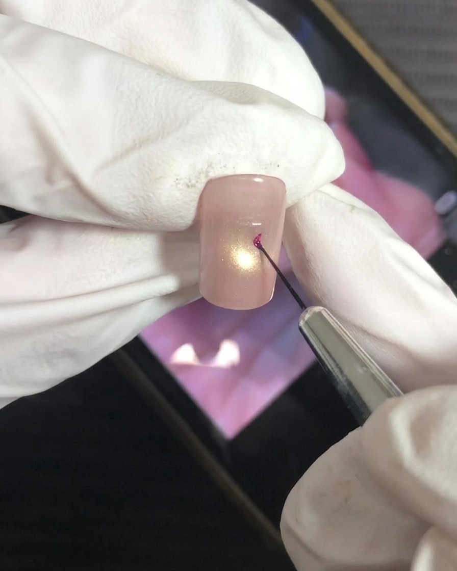 A fine liner brush carefully applying a dot of magenta gel to the center of the nail.