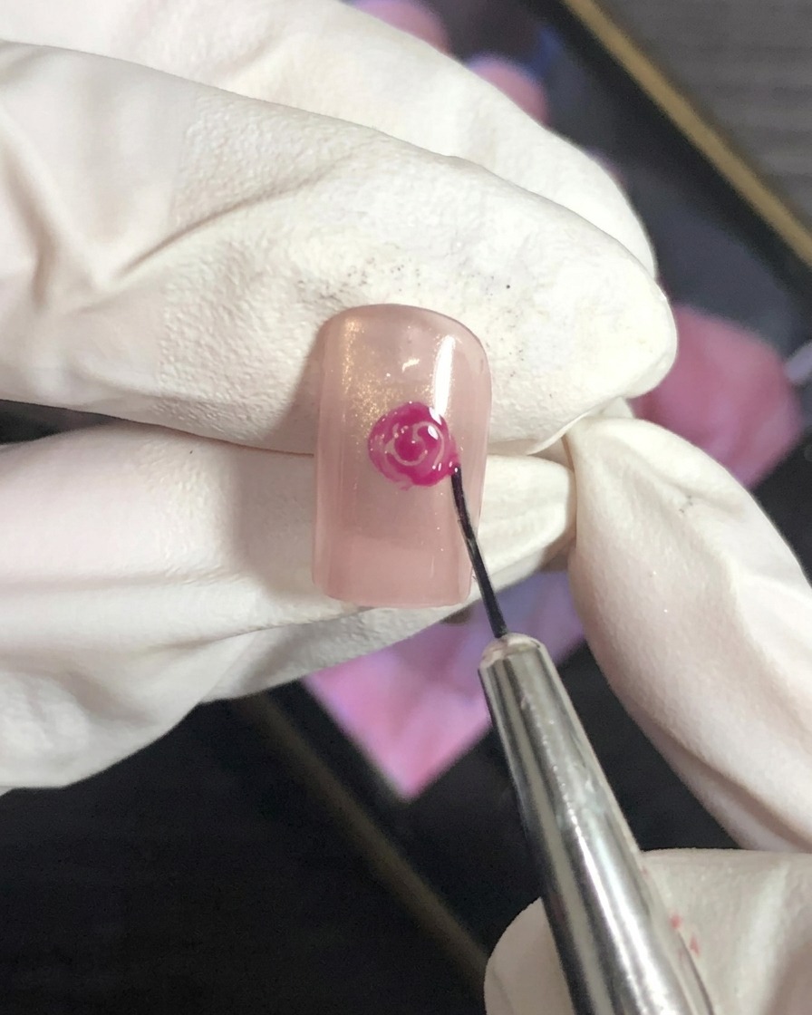 A close-up view of a nail art brush blending the outer edges of a magenta rose petal design on a nude base.