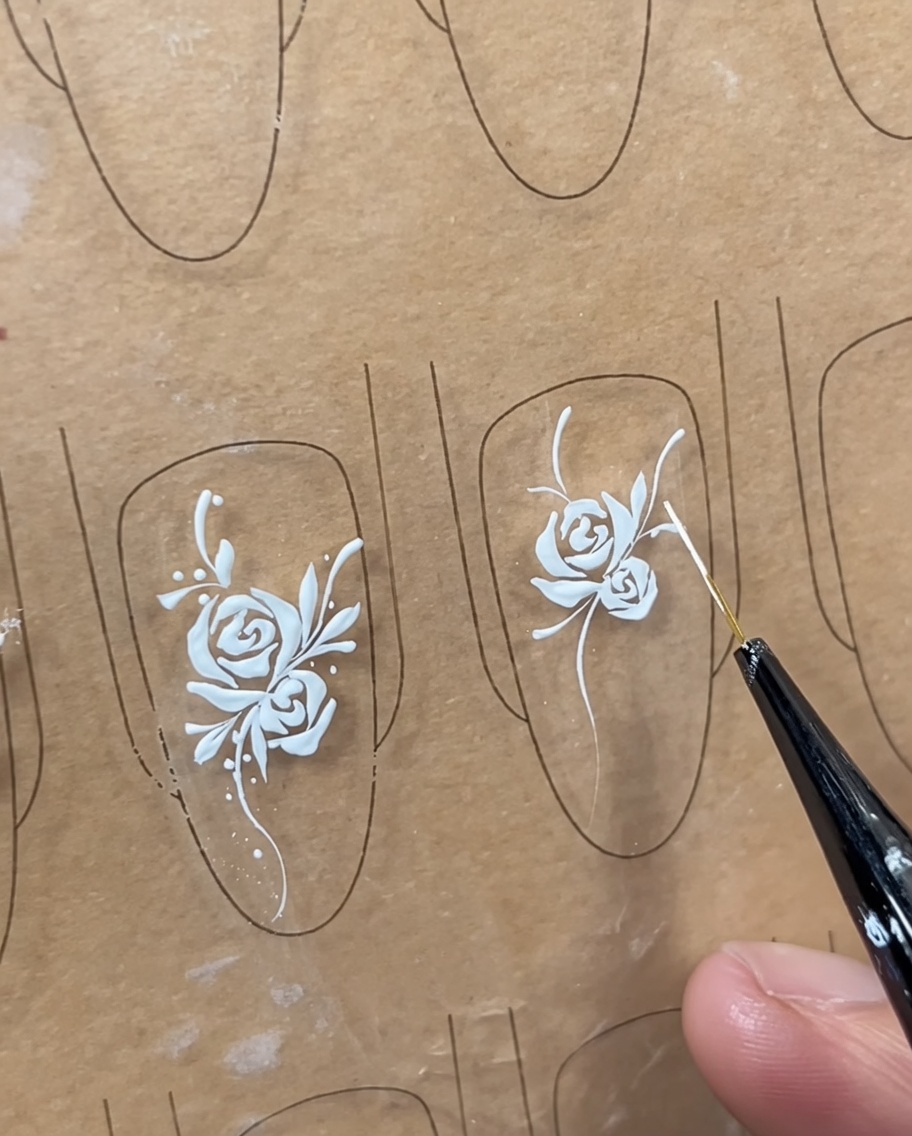 A close-up of a painted white rose on a nail, with additional small highlight strokes added near the center.
