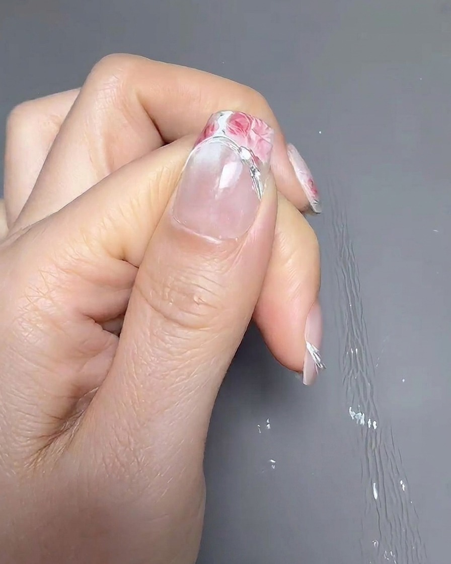 A set of tweezers placing a French tip guide sticker onto the nail plate, positioned slightly higher than normal.