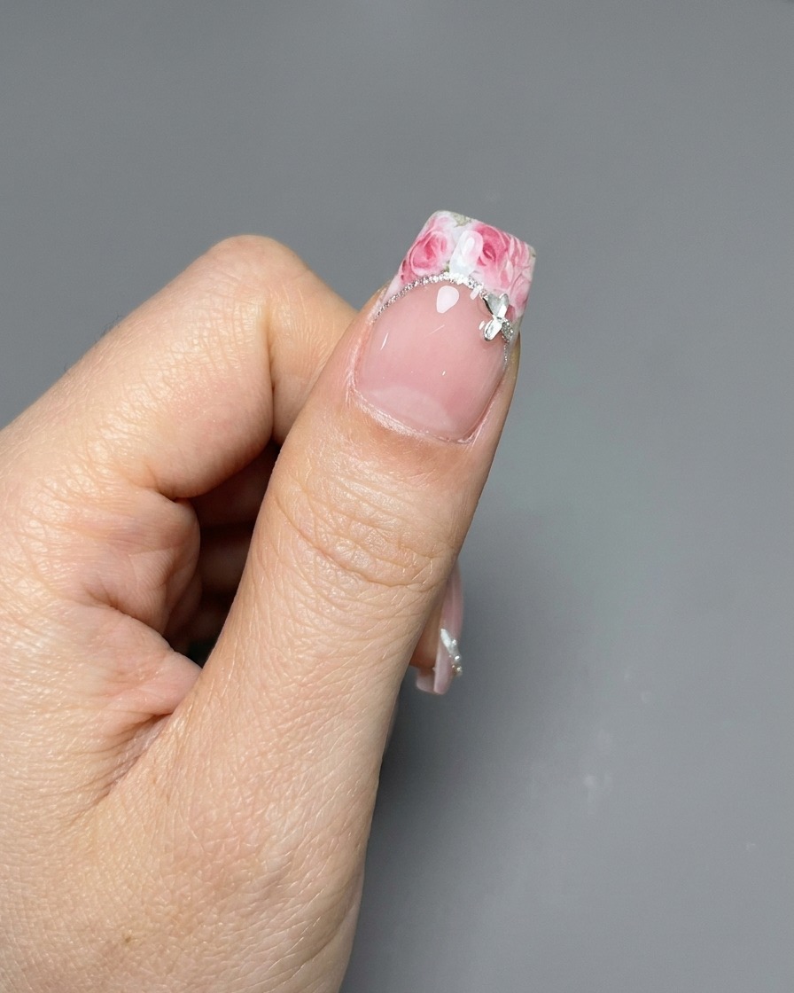 A pair of tweezers placing a rose-patterned sticker onto a manicured French tip.