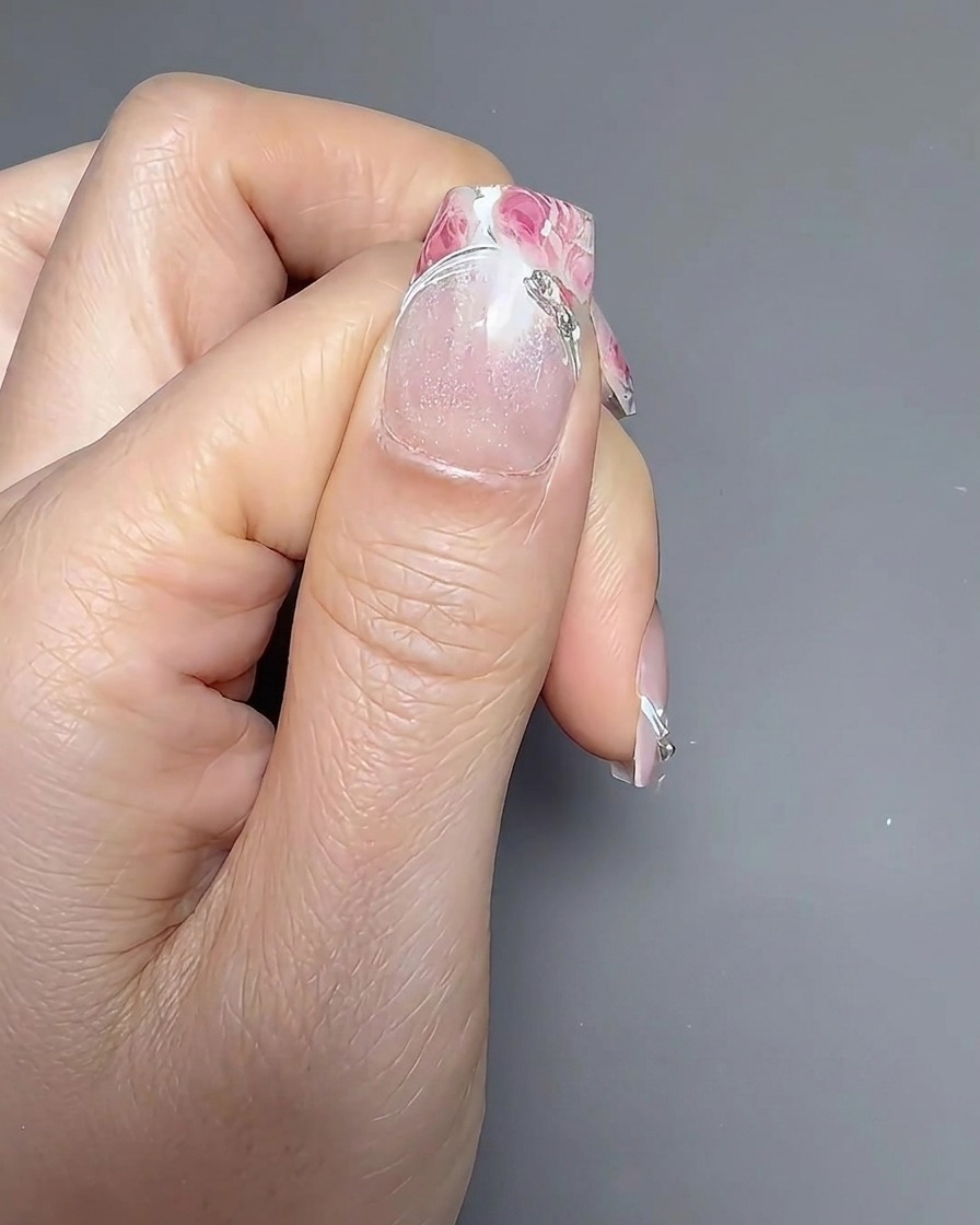 A nail brush applying a clear, glossy top coat over a floral-decorated nail.