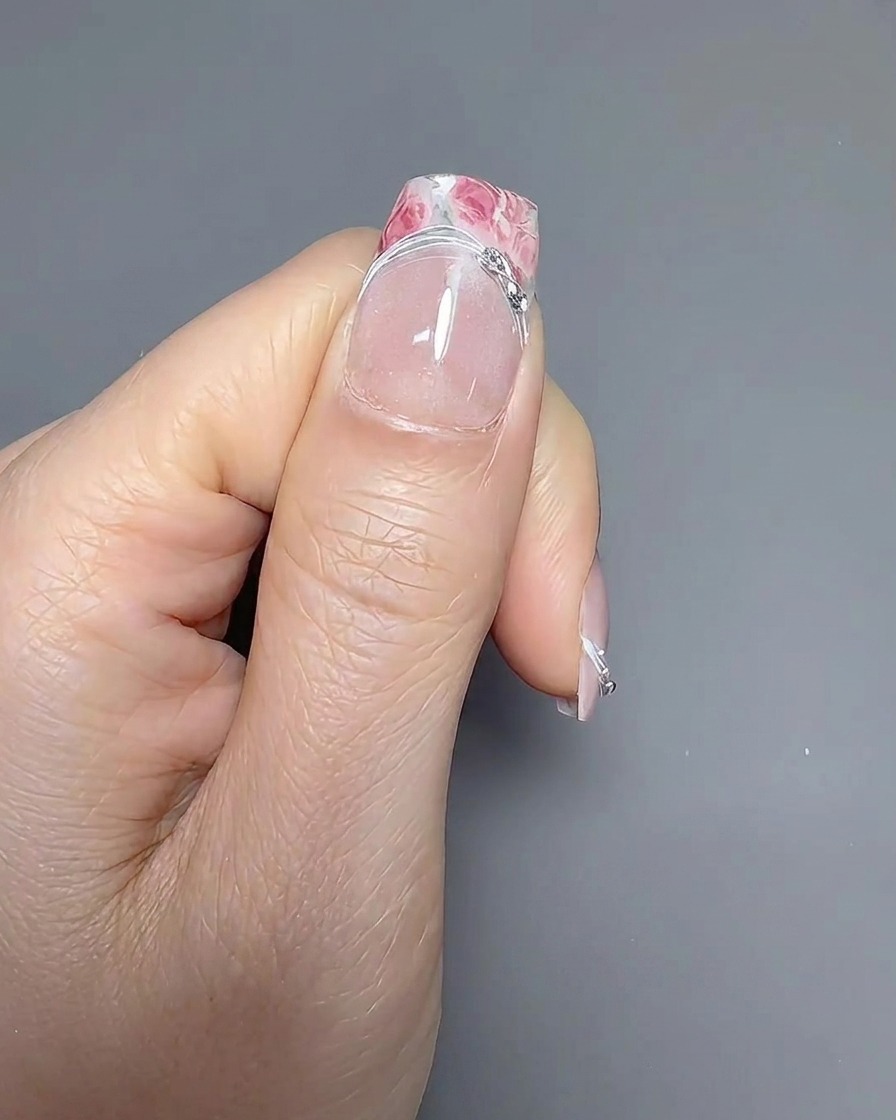 A thin liner brush carefully tracing the smile line on a French manicured nail.