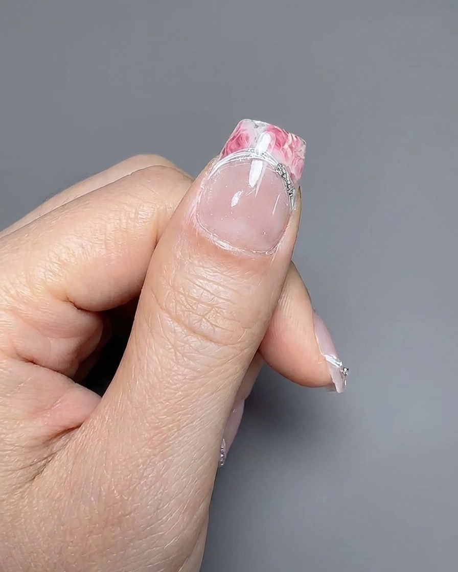Tweezers placing a small silver charm on the intersection of the French tip border line.