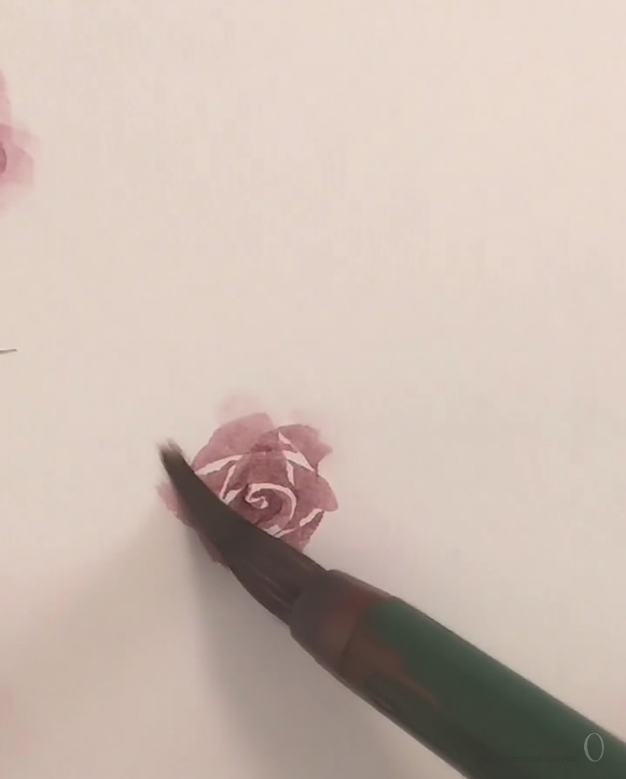 A small brush applying delicate pink watercolor paint to form the final outer petal of a rose.