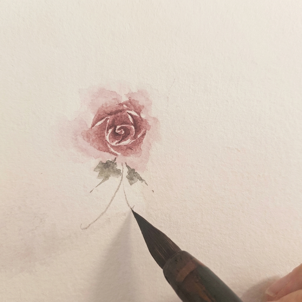 Two small green watercolor leaves painted at the base of a finished rose.