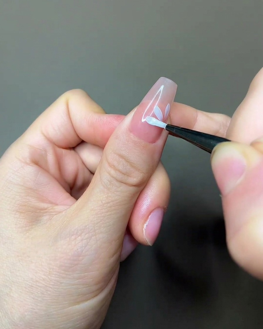 A nail brush applying a coat of matte top coat over a partially painted floral design on a nude nail.