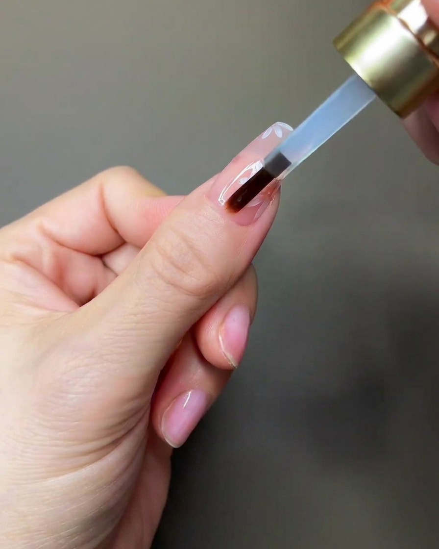 A hand placing a nail under a small portable UV/LED lamp for curing.