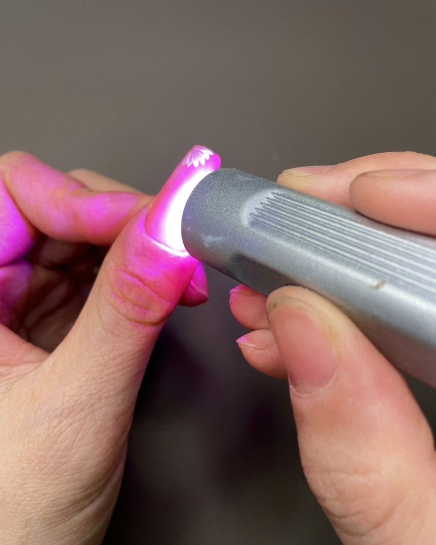 A nail art tool applying a small dot of clear sculpting gel to the nail surface near the painted flowers.