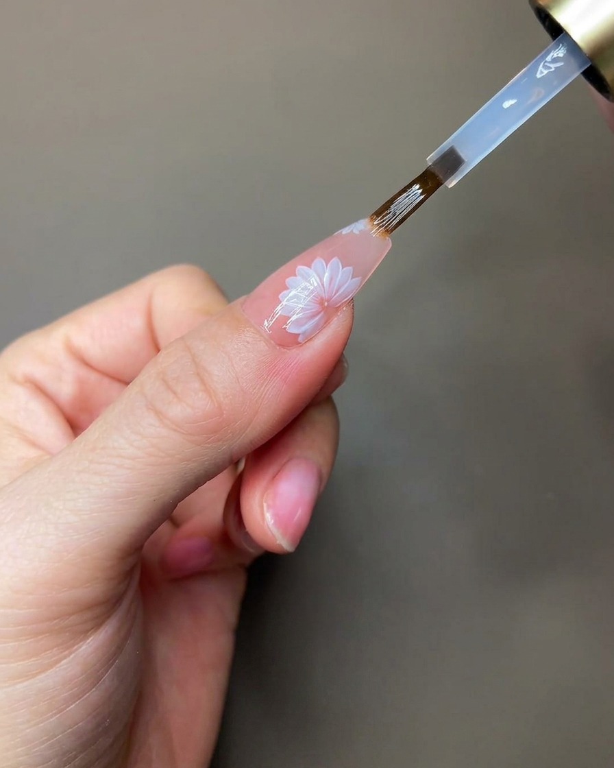 A hand positioned under a portable UV/LED lamp while curing the clear sculpting gel details.
