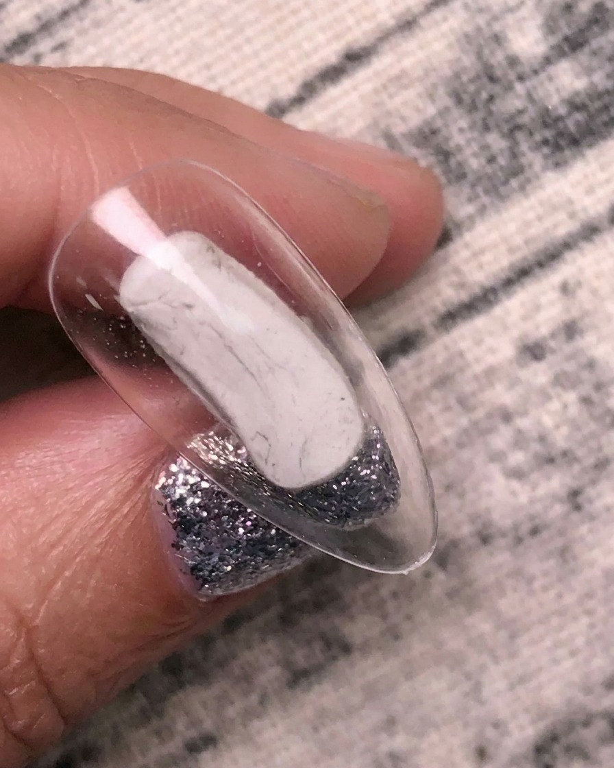 A brush applying a clear transfer adhesive gel to a clear nail tip.