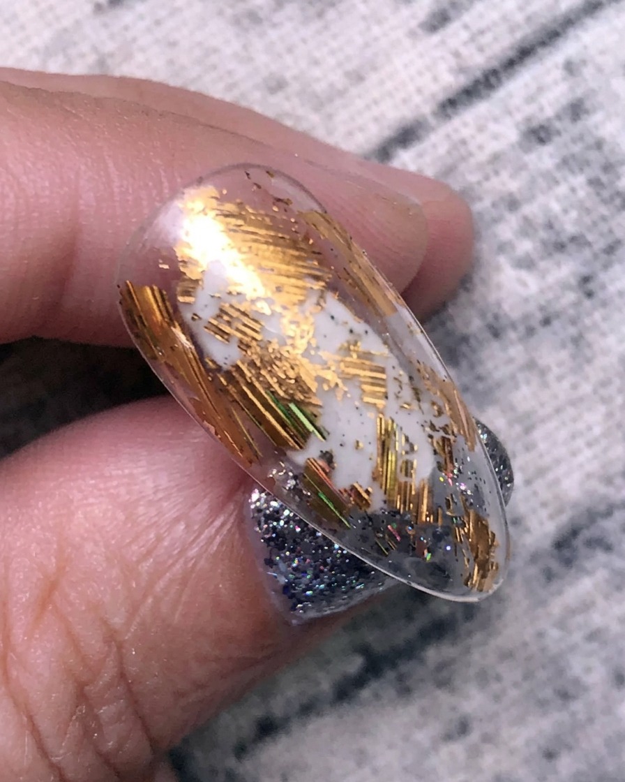 Applying gold transfer foil to a nail surface using a silicone tool.