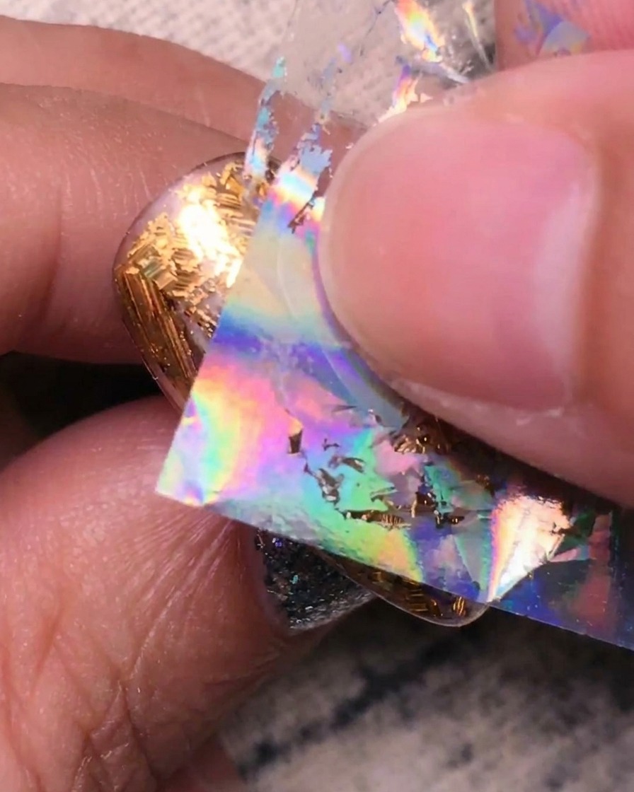 Pressing holographic silver foil onto the remaining clear sections of the nail.