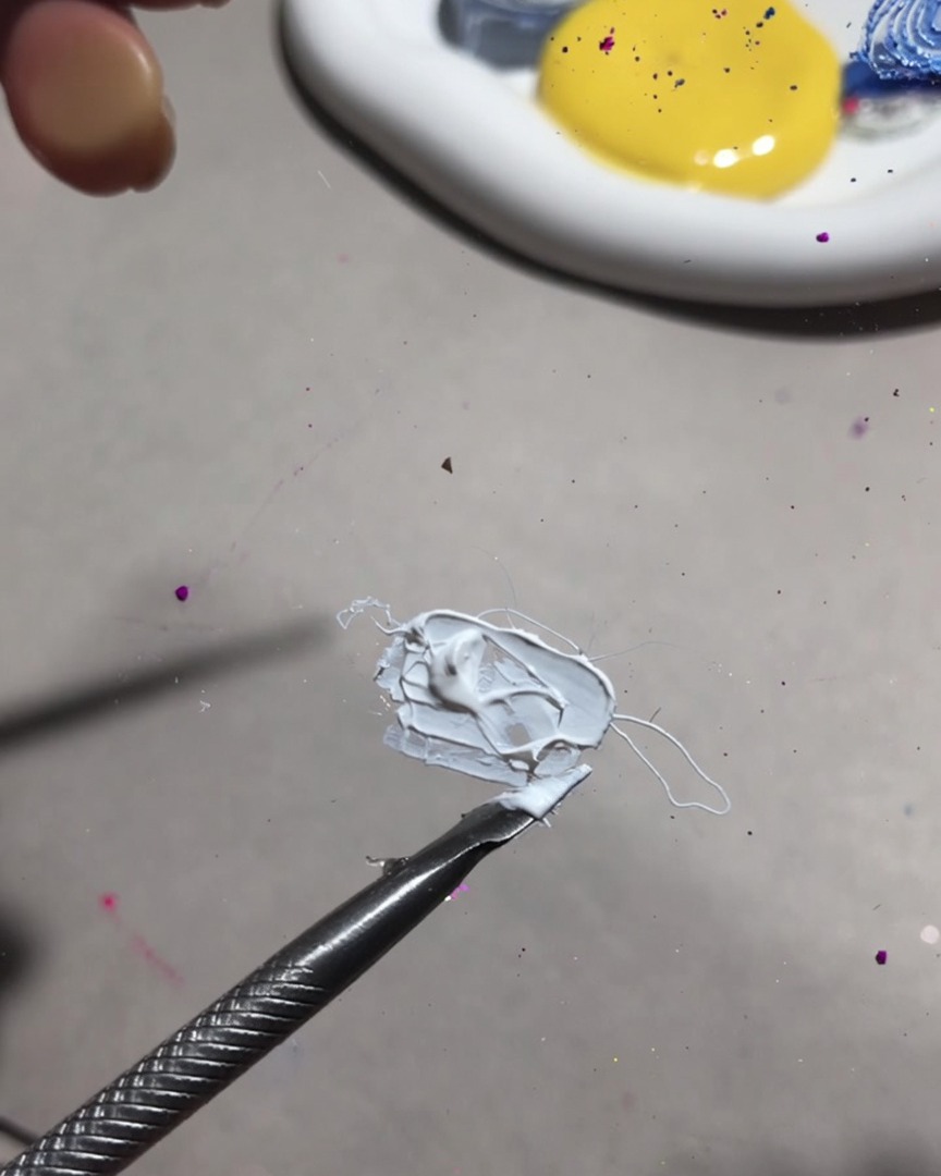 A close-up of a mixing tool blending white painting gel and fruit gel into a smooth, creamy texture.