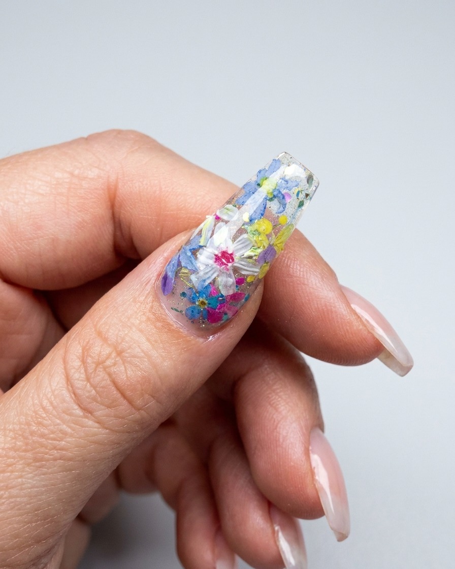 A close-up view of a brush applying multi-colored 3D floral petals onto a decorated nail surface.