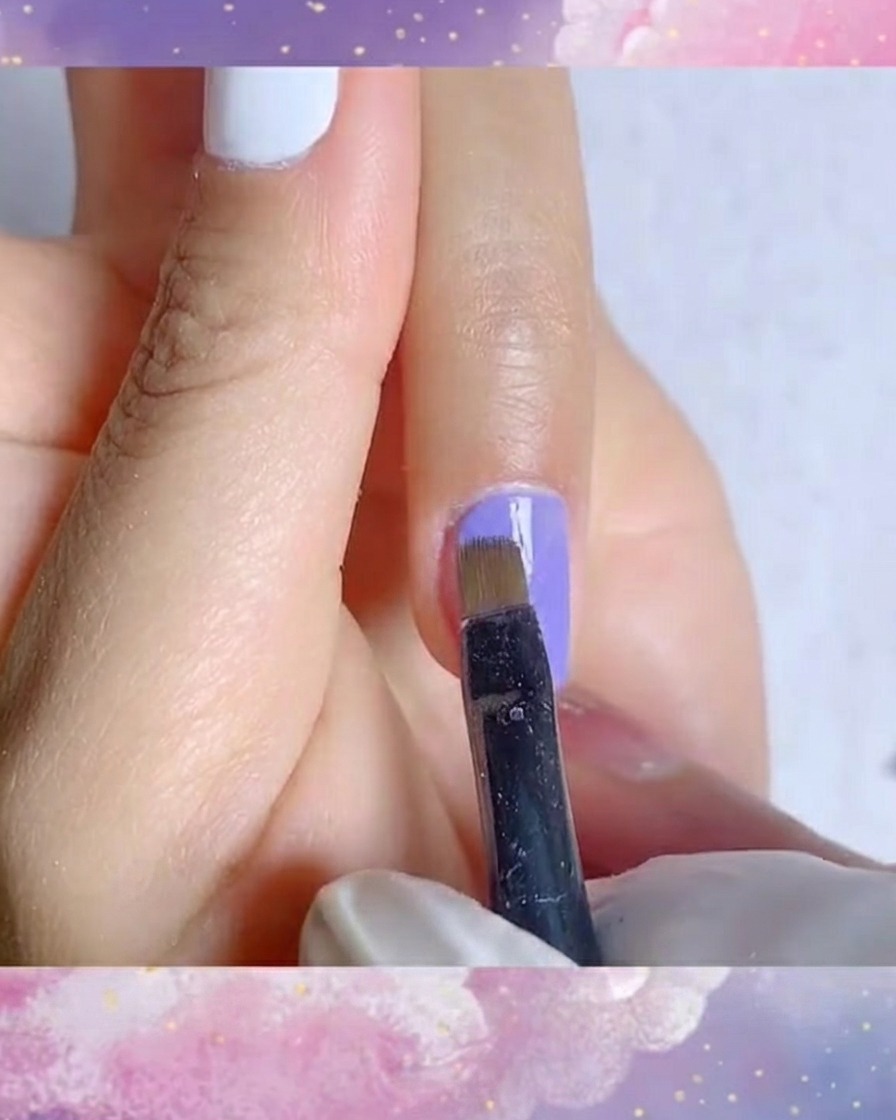 A detailed close-up of a liner brush applying a smooth second coat of vibrant blue-purple gel polish.