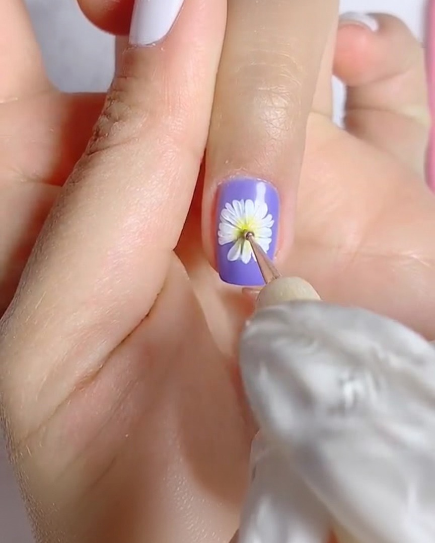 A close-up of a liner brush applying minute brown detail to the yellow center of a painted daisy.