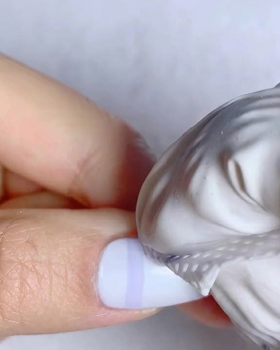 A thin liner brush drawing vertical blue lines on a white nail.