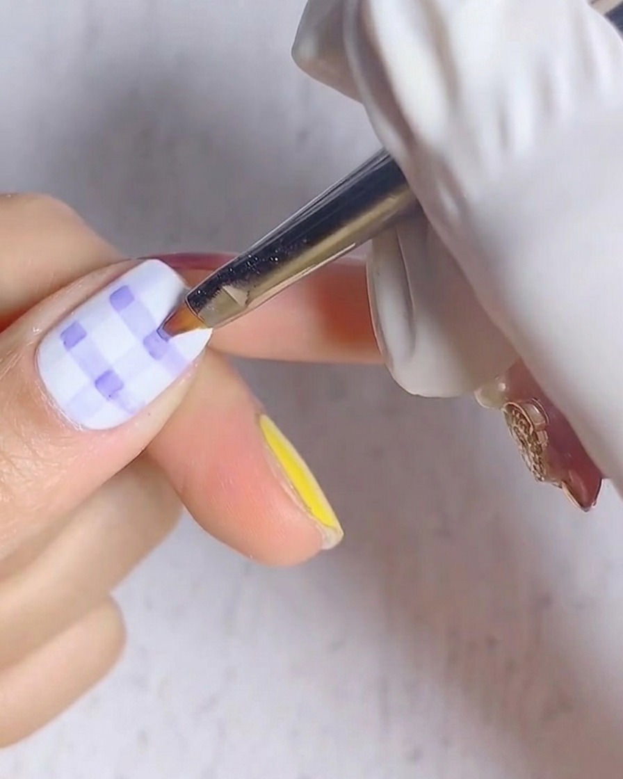 A close-up view of a fingernail with a blue and white plaid pattern placed under a UV nail lamp.