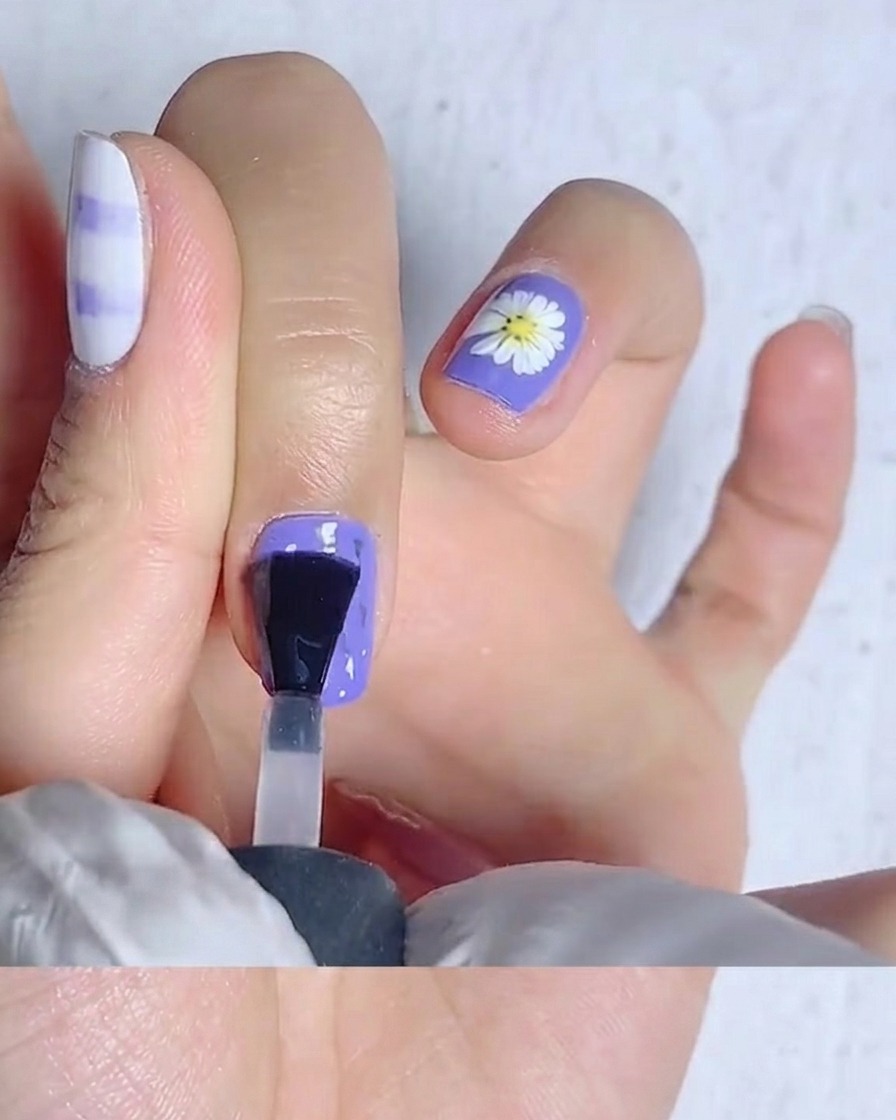 A nail brush spreading matte top coat over a bright yellow nail.