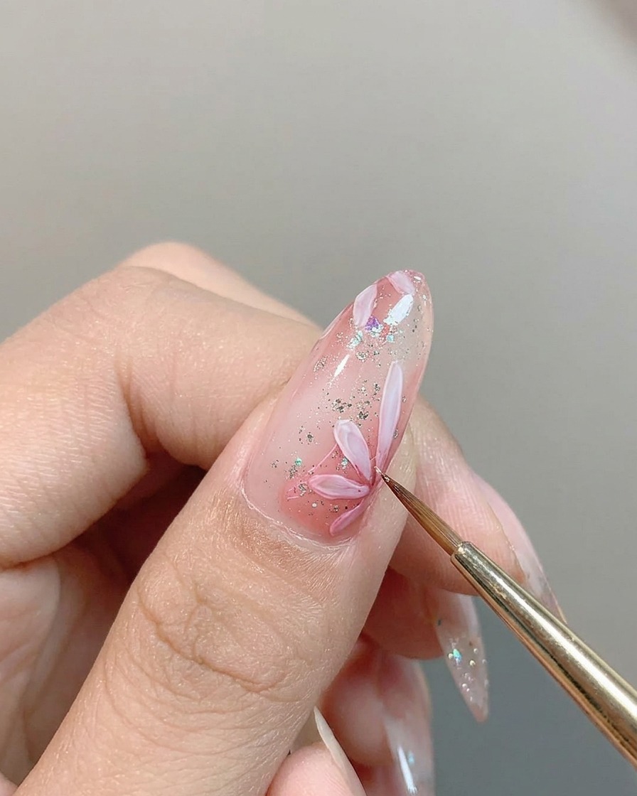 A fine brush dabbing a concentrated spot of pink pigment into the center of a white daisy painted on a nail.