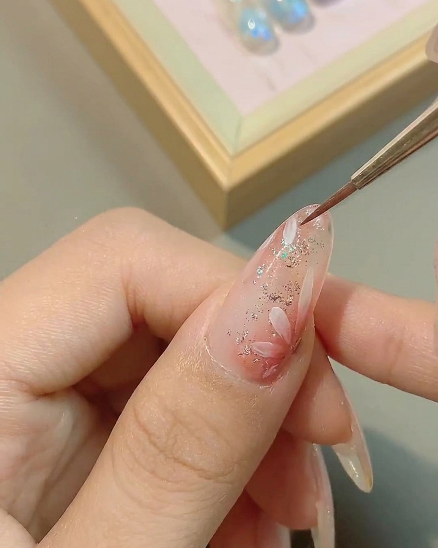 A brush applying a clear, glossy top coat over the finished daisy nail art, smoothing out the surface.
