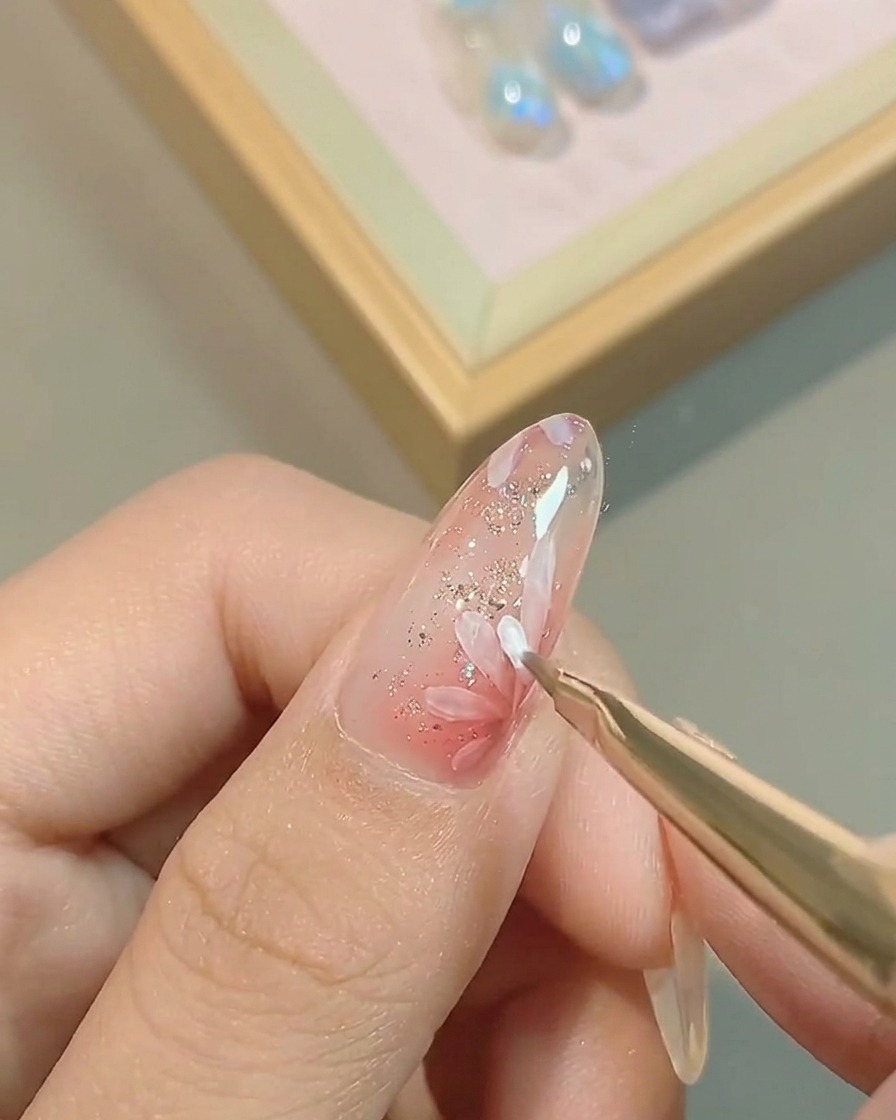 A fine liner brush adding a second layer of white petals, layered over the initial flower design on a pink nail.