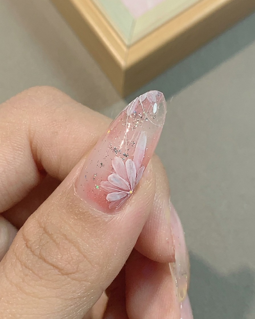 A close-up of a nail with pink daisy petals being refined with a fine liner brush.