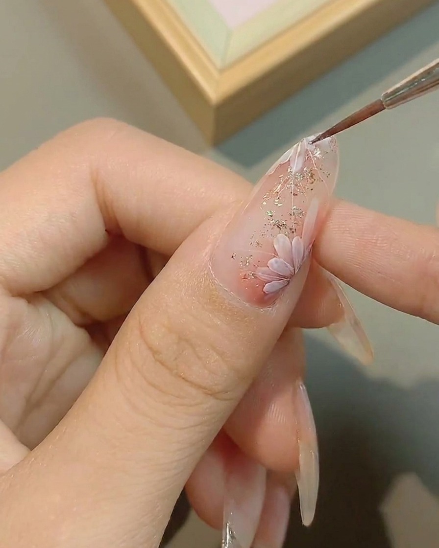 A fine brush adding precise details to the center of a painted daisy.