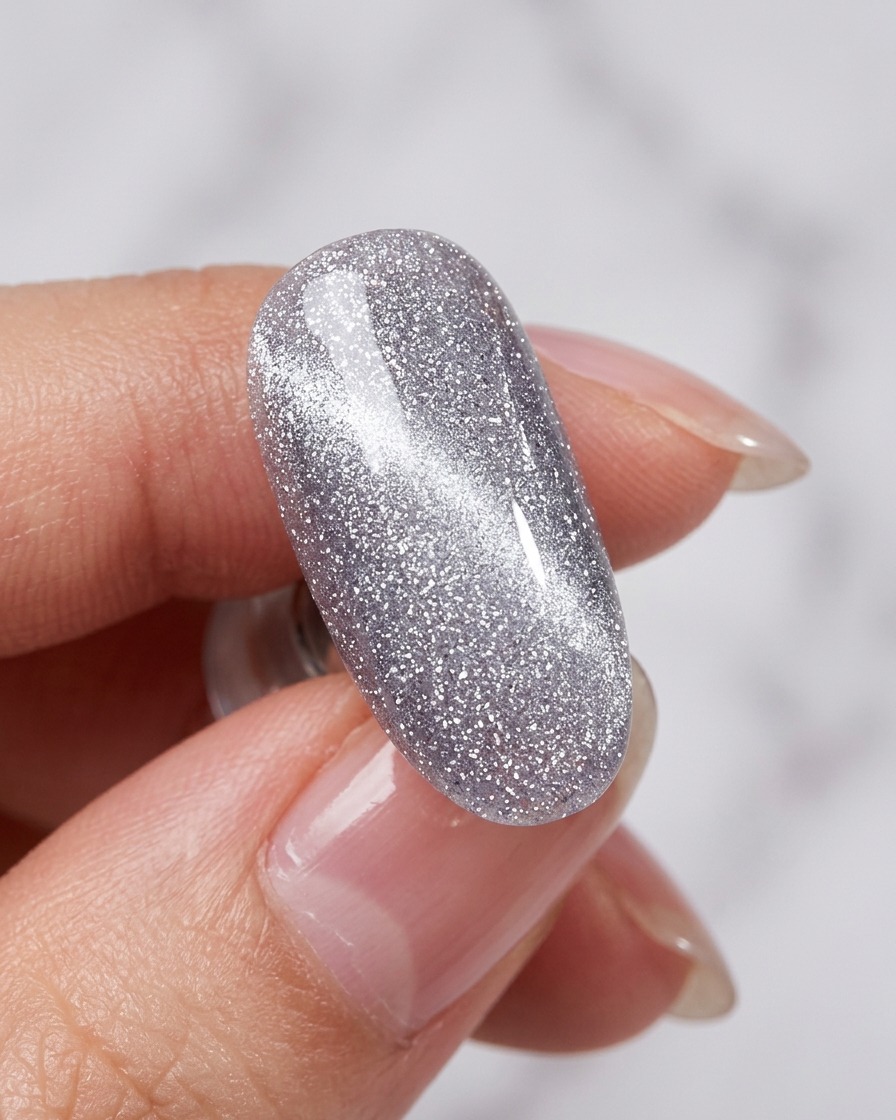A magnet tool being held near a nail coated in wet silver cat-eye polish, revealing a bright shimmering line.